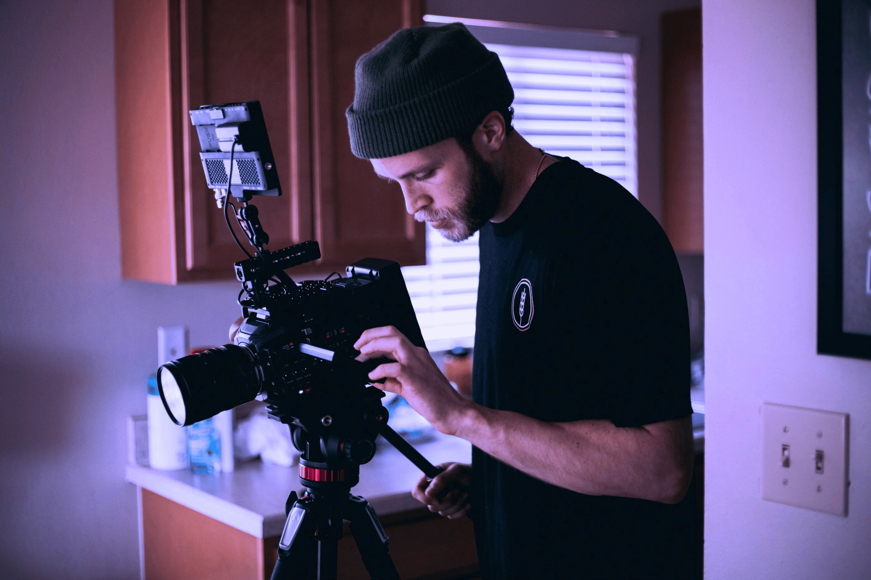Man looking through lens of a camera staged on a tripod within a home